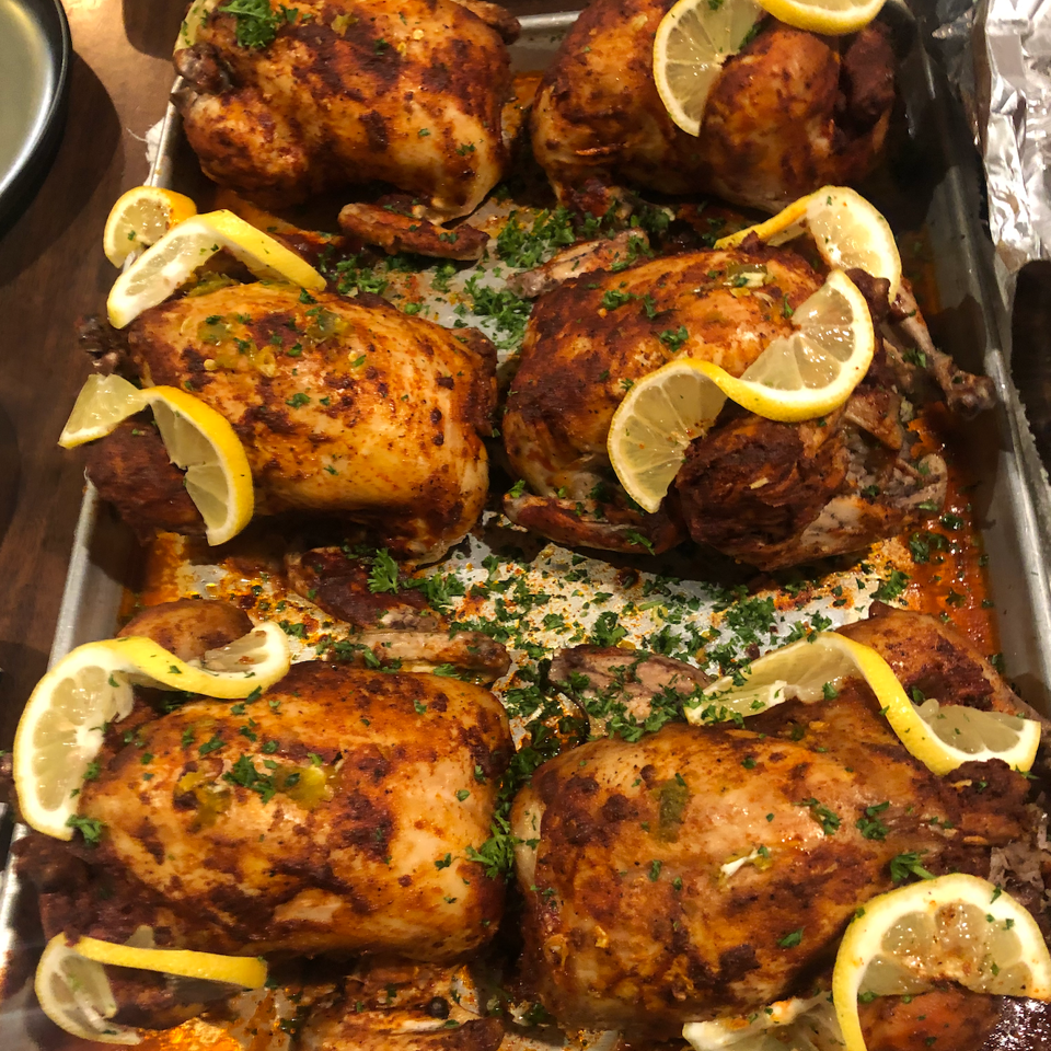 Roasted whole chickens arranged on a platter with lemon wedges, chopped parsley, and savory juices.